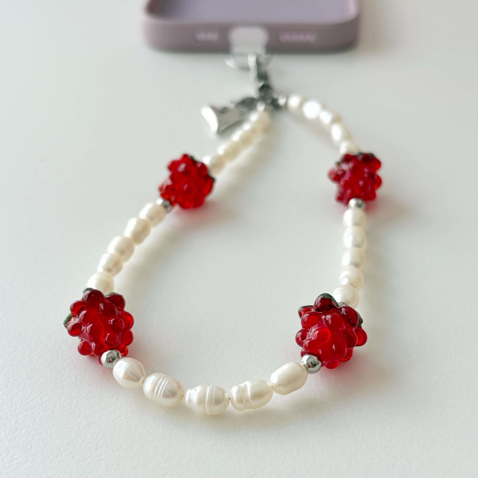 Juicy Pearl phone lanyard strap displayed on flat background with red raspberries and pearls