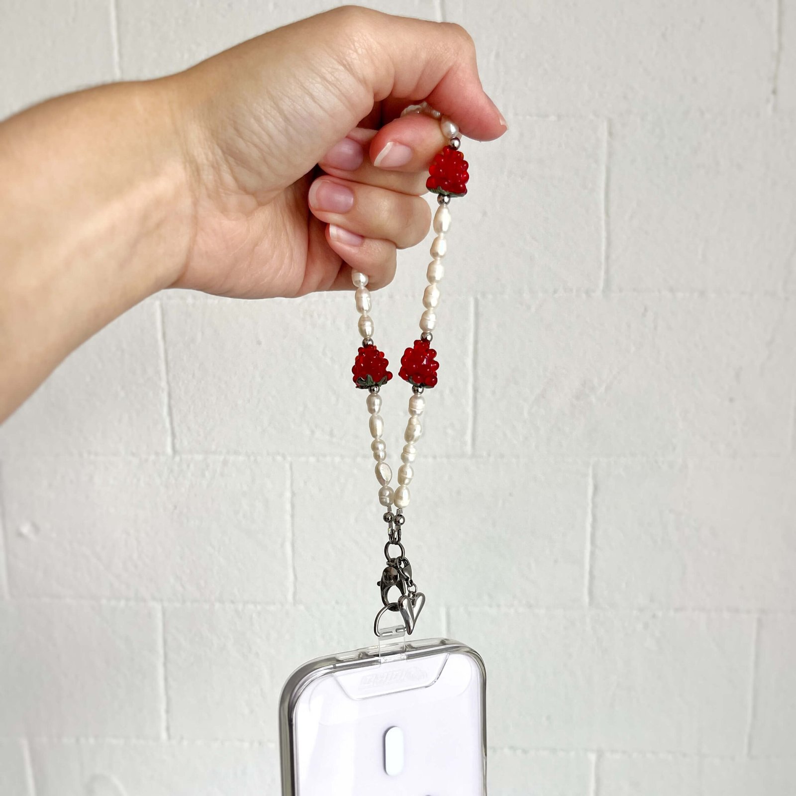 Hand holding Juicy Pearl beaded phone strap showing raspberry glass beads and pearls
